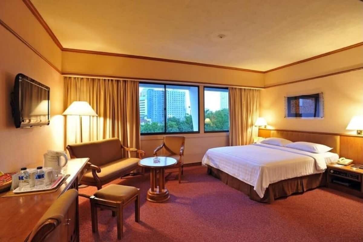 Ett hotellrum med en säng, ett skrivbord, en stol, ett litet bord, en tv och ett fönster med gardiner.