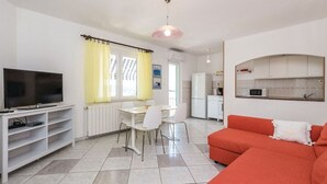 Una sala de estar con televisor, un comedor con sillas, una cocina con microondas y un sofá rojo.