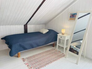 Ein Schlafzimmer mit Bett, Nachttisch, Lampe und Blick ins Freie durch ein Fenster.