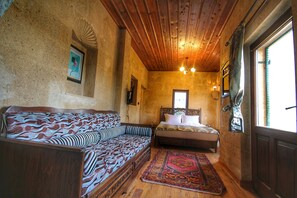 A room with a wooden ceiling, a bed with a patterned bedspread, a sofa with a wavy design, and a traditional rug. - Lovely Cappadocia (Ürgüp)