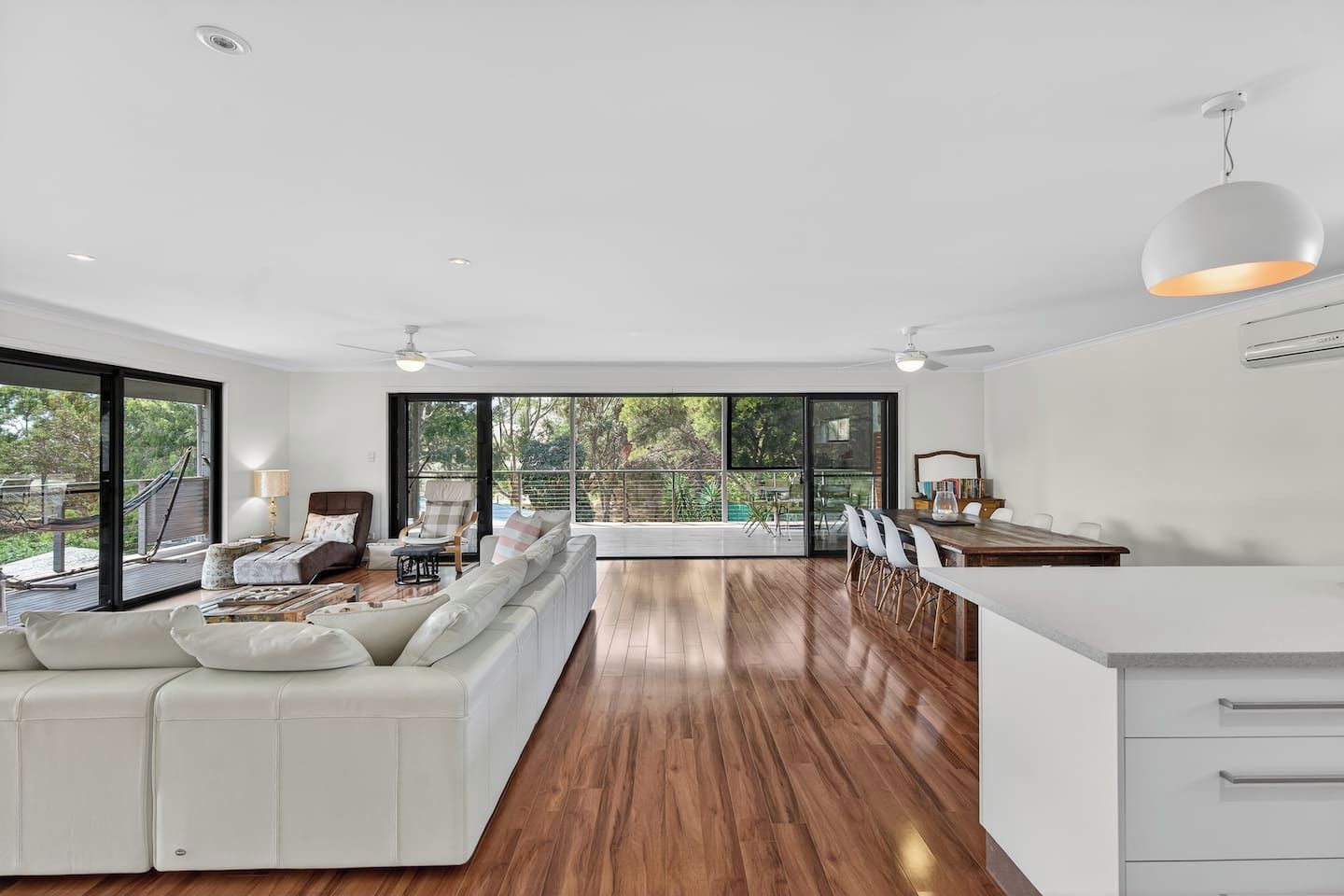 Una sala moderna con un sofá blanco, piso de madera y un comedor con una mesa y sillas blancas.