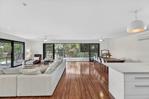 Ein modernes Wohnzimmer mit einem weißen Sofa, Holzboden und einem Essbereich mit weißem Tisch und Stühlen.