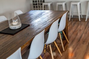 A wooden dining table with white chairs, a candle, and a black placemat. - Swell Beach House - Families Walk to the Beach (Second Valley)