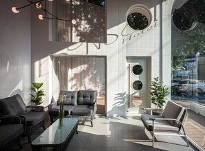 Eine moderne Hotelhalle mit Sitzgelegenheiten, einem Glastisch und einem großen Fenster mit Blick ins Freie.