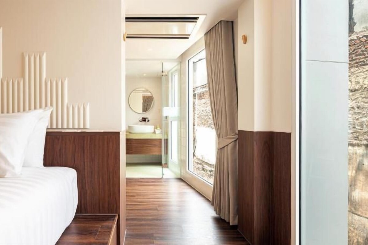 Una habitación de hotel con cama, baño con lavamanos y espejo, y vista por la ventana.