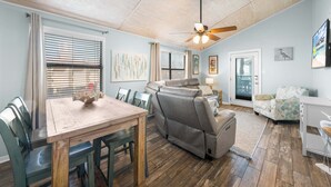 A spacious living area with a dining table, a sofa, a recliner, and a ceiling fan. - Lani Kai 230 Gulf Coast Condo. Walk to Beach + Pools + Balcony Views! (Gulf Shores)