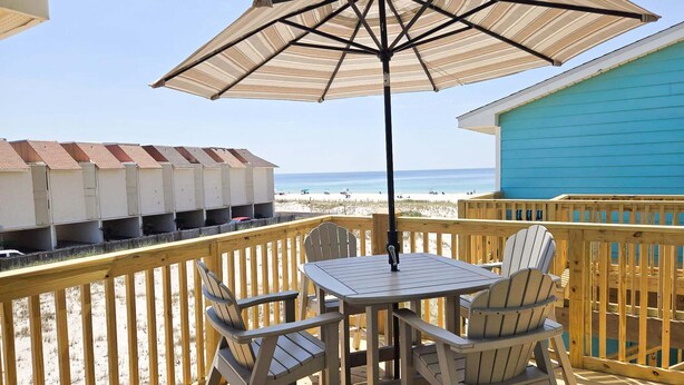 A wooden deck with a table and chairs, a striped umbrella, and a view of the beach and ocean. - Lani Kai 230 Gulf Coast Condo. Walk to Beach + Pools + Balcony Views! (Gulf Shores)