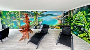 A room with a beach mural, a wooden sculpture, and two black lounge chairs. - Puffin - Laïta (Guidel)