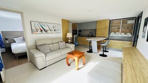 A modern hotel room with a sofa, a wooden coffee table, a dining area with a table and chairs, a kitchen area, and a bed with a view. - Puffin - Laïta (Guidel)