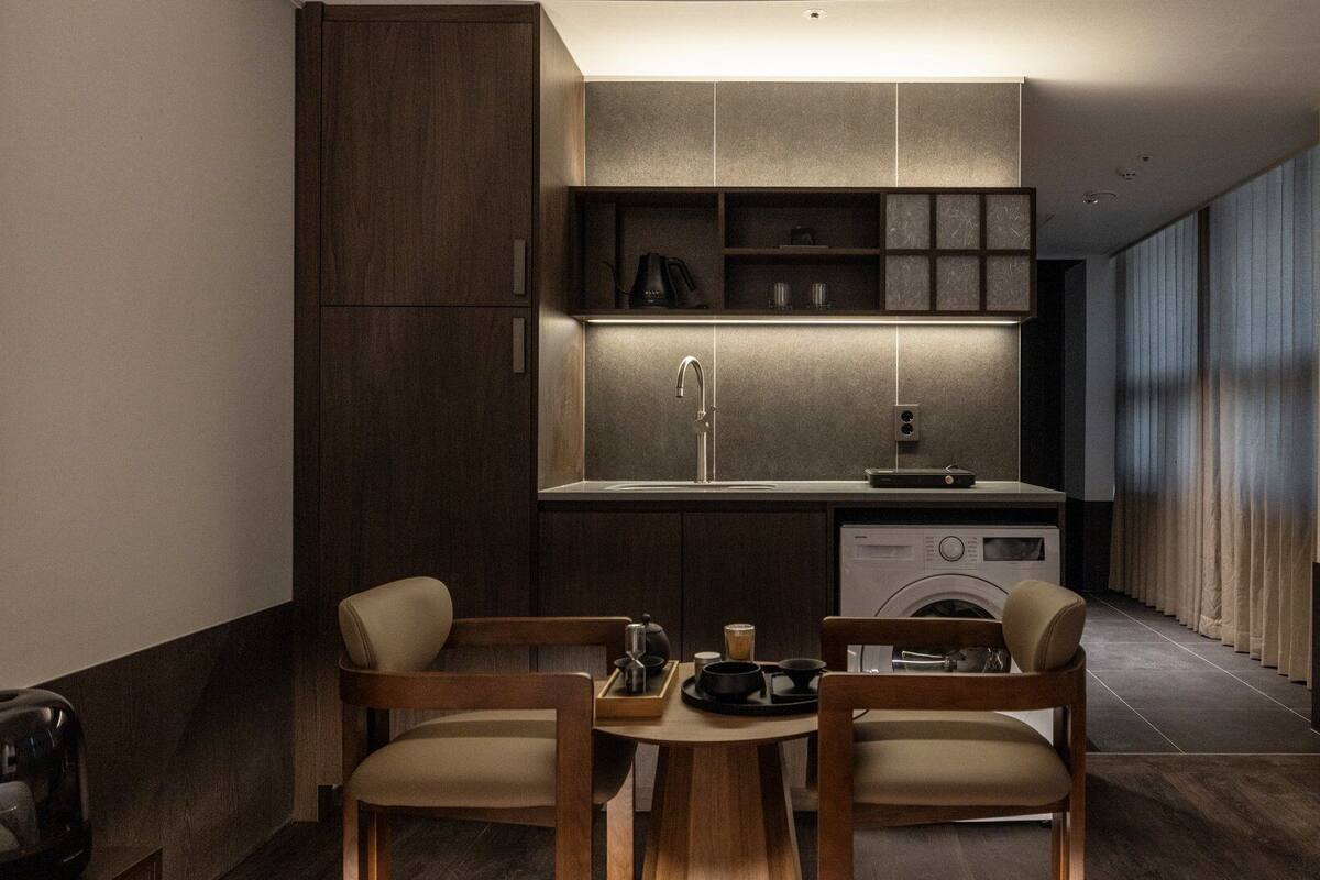 A compact kitchen with modern appliances, a dining area with two chairs, and a washing machine.