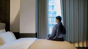 Une chambre d’hôtel avec un lit, une fenêtre avec des rideaux et une vue sur un bâtiment à l’extérieur.