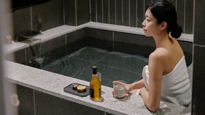 Uma pessoa sentada junto a uma piscina de spa, com uma garrafa de azeite e um tabuleiro com comida.