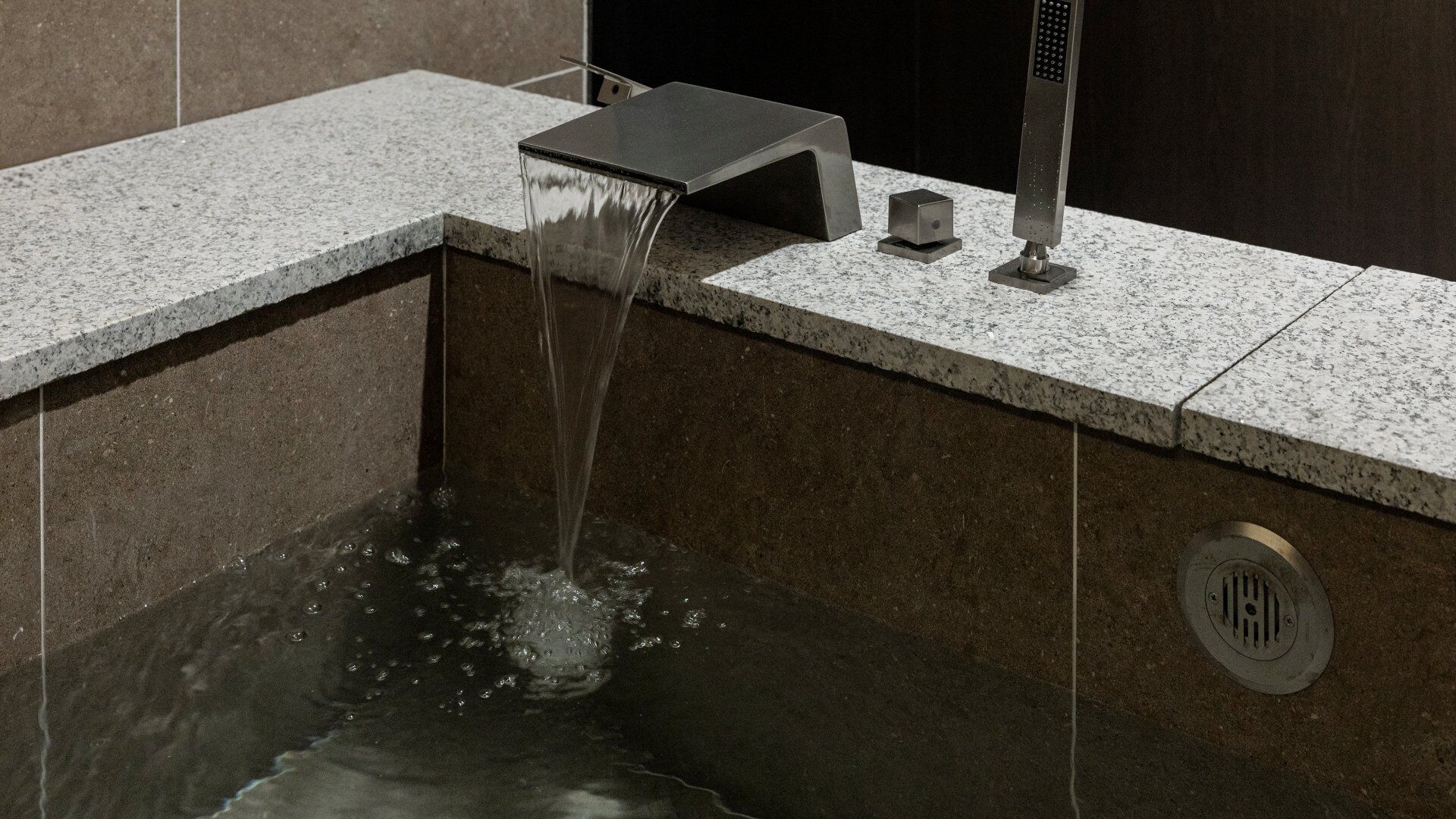 A modern bathroom with a square sink, a faucet, and a drain.