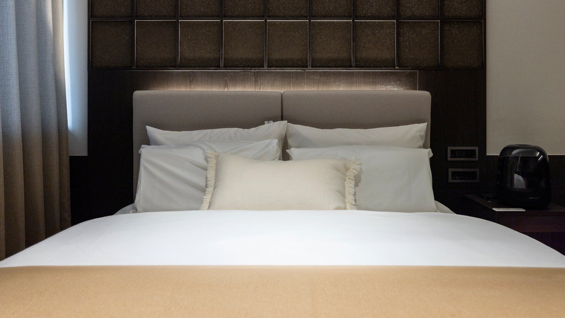 A hotel room with a bed, a headboard, a nightstand, and a coffee maker.