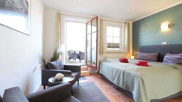 Ein Hotelzimmer mit Bett, Sofa, kleinem Tisch, Balkon mit Stuhl und Fenster.