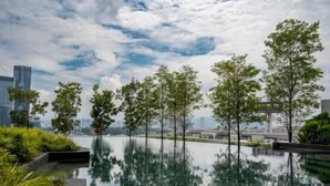 Un cos d'aigua tranquil·la que reflecteix arbres i edificis, envoltat de vegetació.
