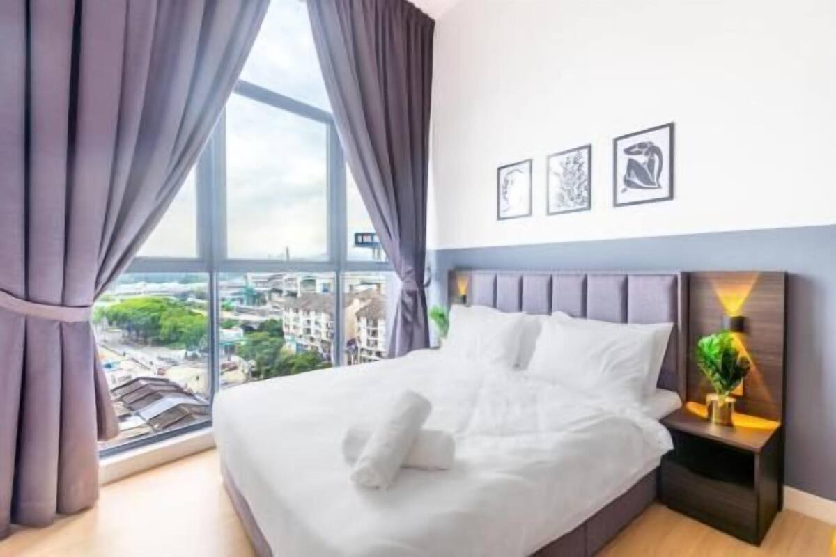 Ein Hotelzimmer mit großem Fenster, einem Bett mit weißer Bettwäsche, einem Nachttisch mit Lampe und drei gerahmten Bildern an der Wand.