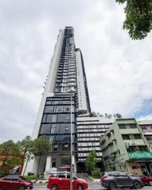 Um edifício alto e moderno com design vertical marcante, com vários andares e uma combinação de elementos de fachada em vidro e painéis sólidos.