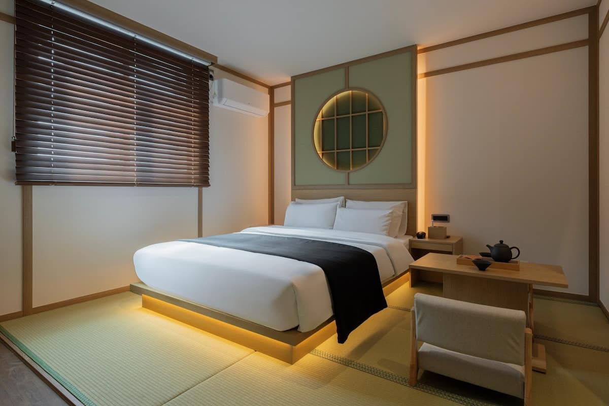 A hotel room with a bed, bedside table, and a small desk with a chair.