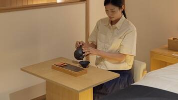Una persona sirve té en una taza sobre una mesa de madera en una habitación con una cama y una mesita de noche.