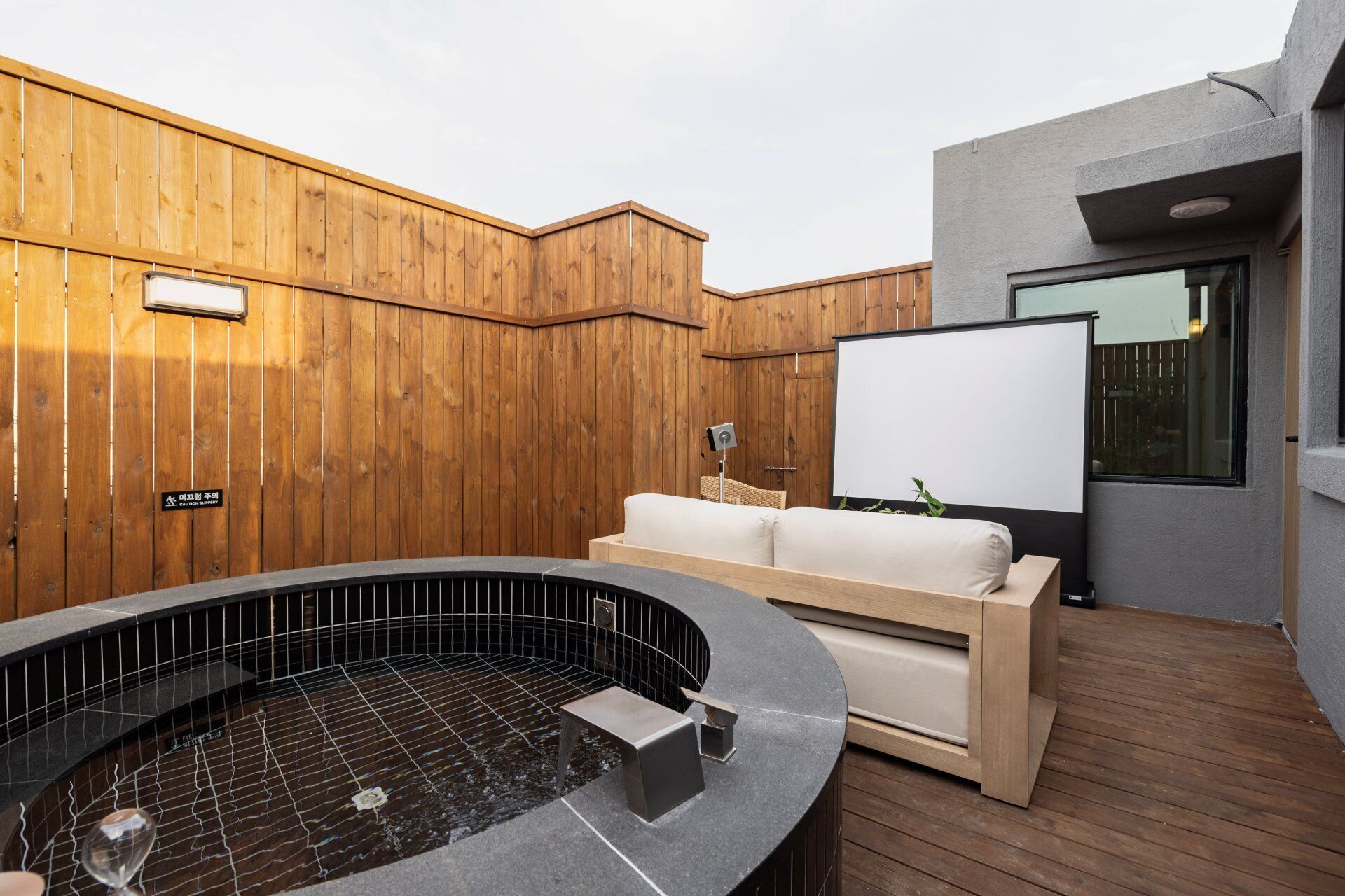 Un jacuzzi con cubierta de madera, un sofá blanco y una pantalla de proyector.