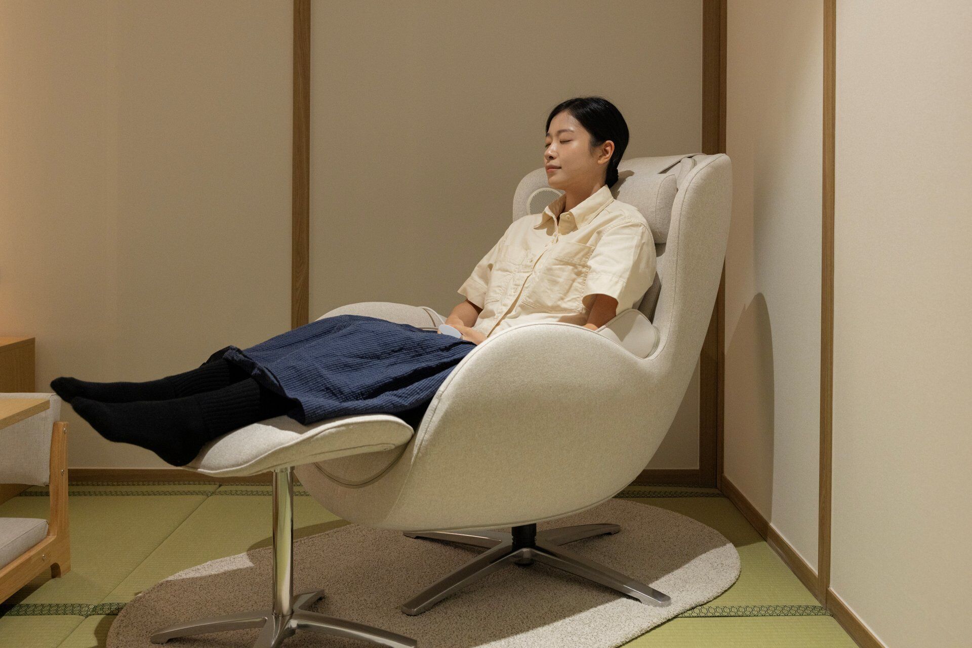 Una persona sentada en una silla moderna con respaldo alto y patas de metal, sobre un suelo de esteras de tatami.