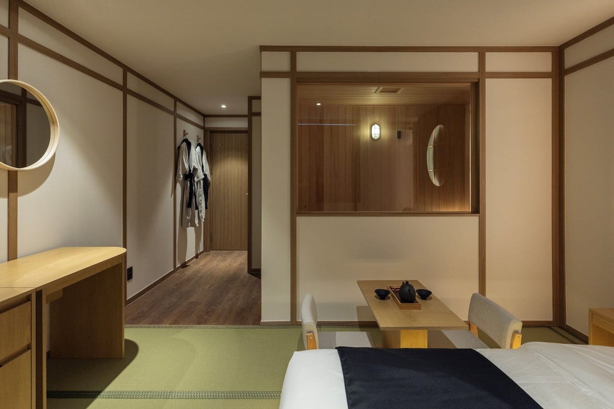 A hotel room with a bed, a desk, a table with a chair, a mirror, and a wardrobe.