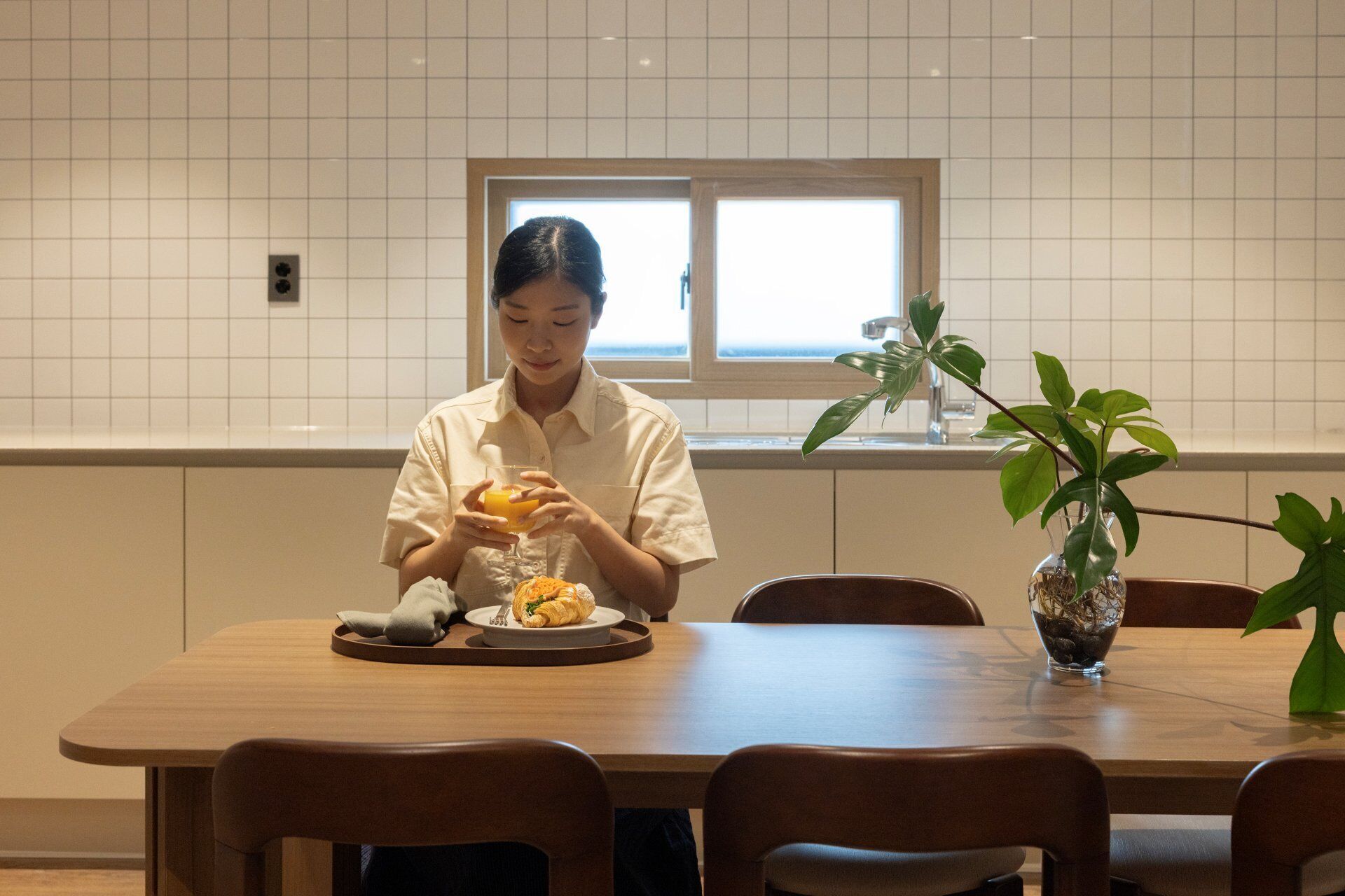 A person seated at a wooden dining table with a plate of food and a glass of orange juice.