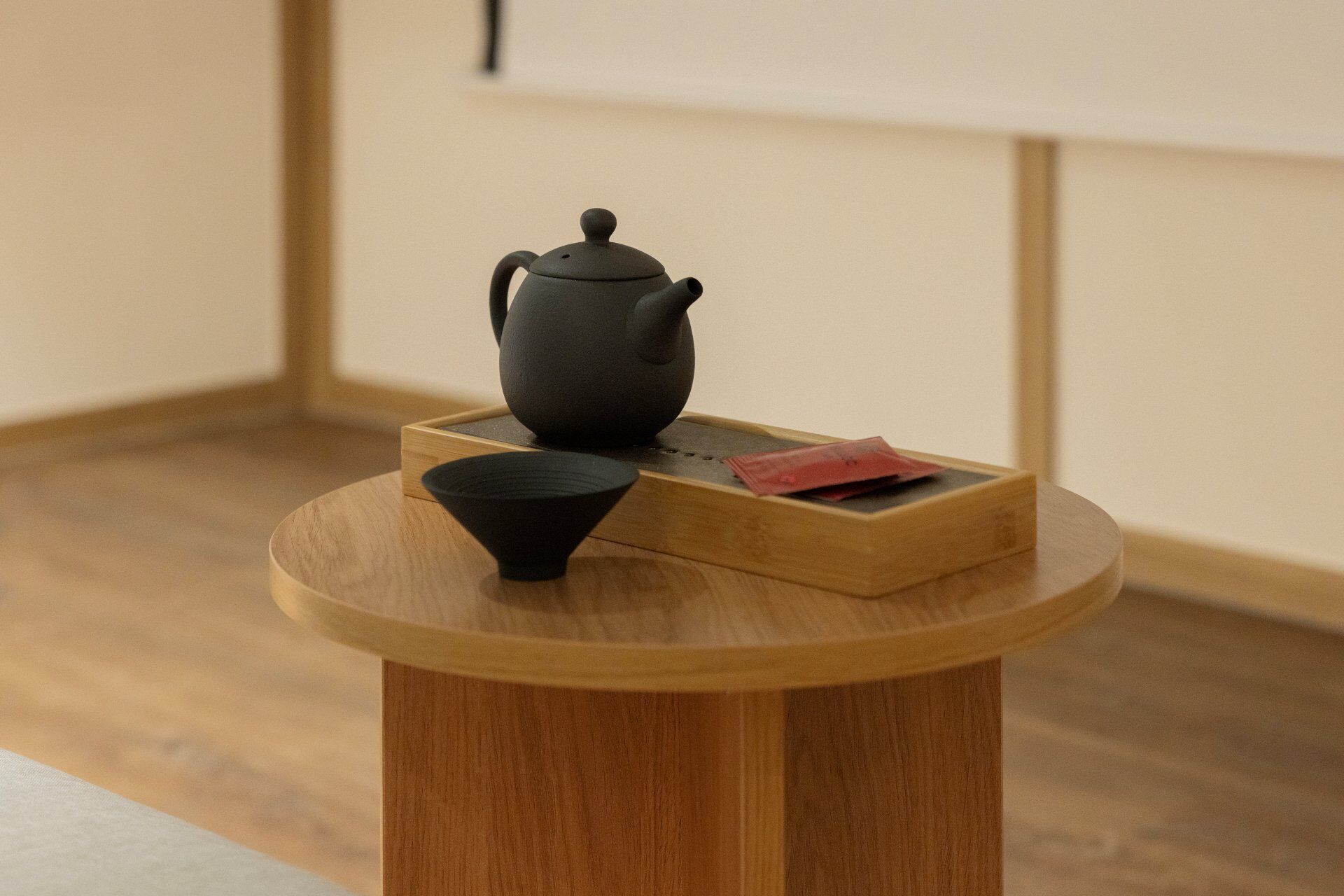 Una mesa redonda de madera con una tetera negra y una taza negra encima.