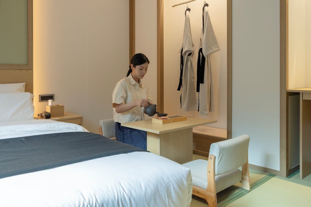 A hotel room with a bed, bedside table, desk, chair, and a wall-mounted towel rack.