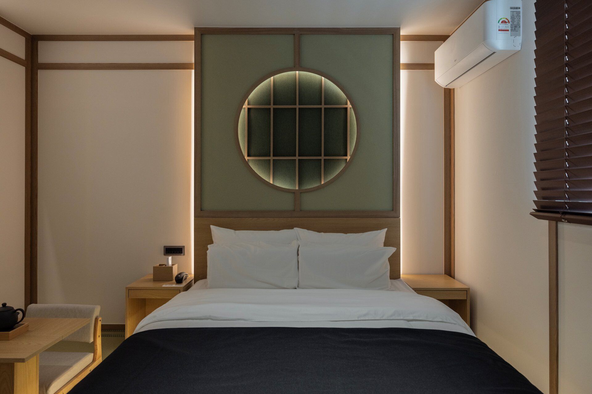 Habitación de hotel con cama, mesitas de noche, aire acondicionado de pared y ventana con persianas.
