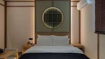 Habitación de hotel con cama, mesitas de noche, aire acondicionado de pared y ventana con persianas.