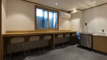 Uma sala de conferências com uma mesa comprida, cadeiras, uma janela, unidade de ar condicionado, pia e frigorífico.