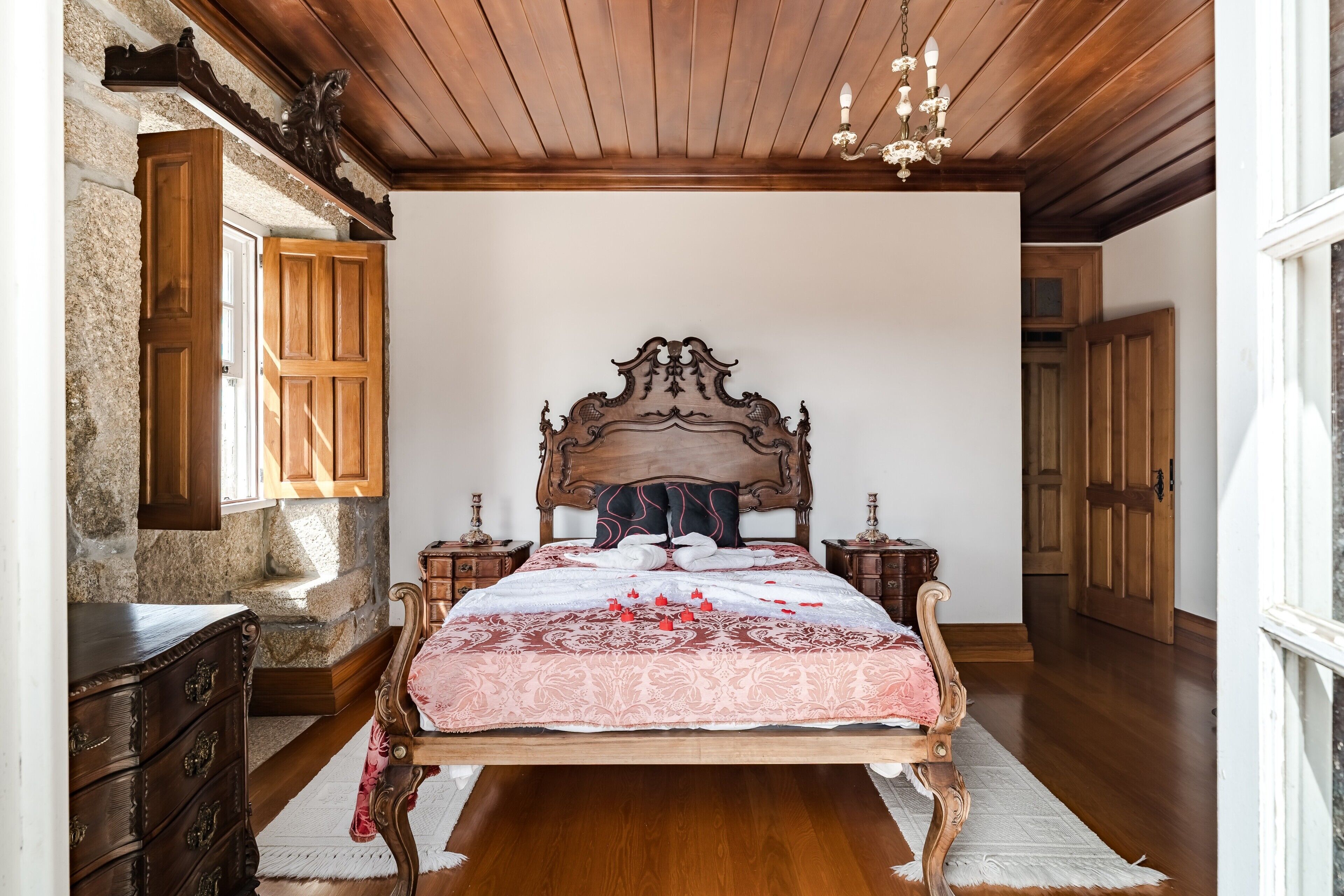 Una camera da letto con un letto grande, una testiera in legno, un muro in pietra, pavimento in legno e un lampadario.