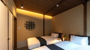 Une chambre d’hôtel avec deux lits, un plafond en bois, une étagère fixée au mur et une table de chevet avec une lampe.