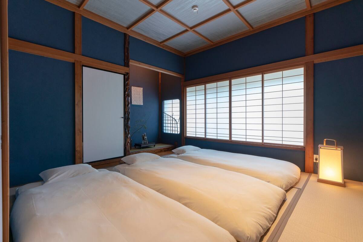 A traditional Japanese-style room with tatami flooring, a shoji screen window, and a futon bed.