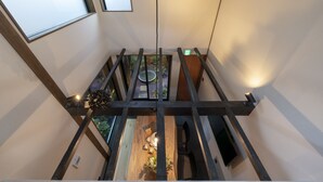 Un intérieur aux hauts plafonds avec des poutres apparentes, un plancher en bois et une vue sur la verdure environnante.