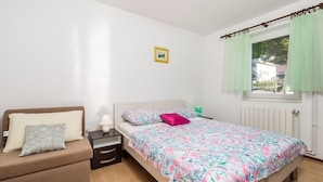 Ein Schlafzimmer mit einem Bett, einem Nachttisch, einer Kommode, einem Fenster mit Vorhängen und einem Bild an der Wand.