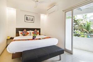 A hotel room with a bed, a bench, a ceiling fan, an air conditioning unit, a framed picture on the wall, and a balcony with a view of palm trees. - Fabexpress Kalyan (Vadodara)