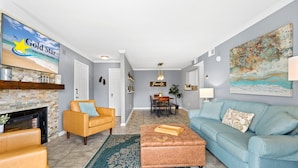 A living room with a fireplace, a sofa, a coffee table, a TV, and a dining area with a table and chairs. - Cozy Condo Near Baseball Fields and Zoo- Pool Tennis Courts Pickleball (Gulf Shores)