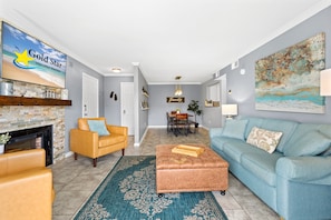 A living room with a fireplace, a sofa, a coffee table, a TV, and a dining area with a table and chairs. - Cozy Condo Near Baseball Fields and Zoo- Pool Tennis Courts Pickleball (Gulf Shores)