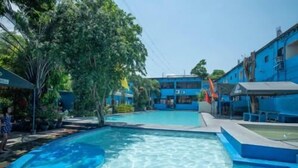Una piscina con agua cristalina, rodeada de edificios azules y árboles.