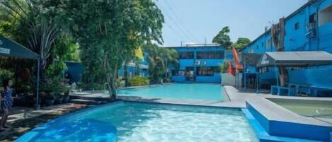 Una piscina con agua cristalina, rodeada de edificios azules y árboles.