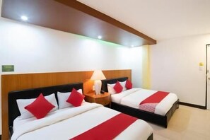 A hotel room with two beds, each with red pillows and a white bedspread. There is a wooden headboard, a bedside table with a lamp, and a door to the right. - OYO 195 Ranchotel - Biã±an (Biñan City)