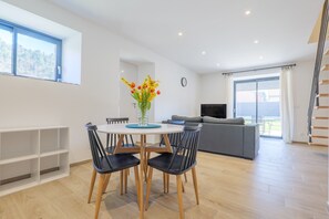 Ein modernes Wohnzimmer mit Essbereich, einer Couch, einem Fernseher und einer Treppe.