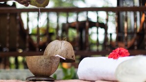 A person squeezing a coconut, a wooden bowl, and a white towel with a red flower on a wooden table. - Amã Stays & Trails Asanji Wadi (Alibag)