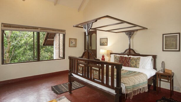A four-poster bed with a wooden frame, a window with a view of trees, and a red lamp on a bedside table. - Amã Stays & Trails Asanji Wadi (Alibag)