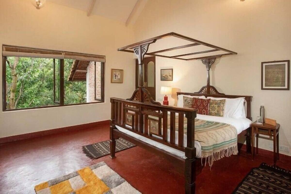 Un dormitorio con cama con dosel, una ventana con vistas a la vegetación y un candelabro.