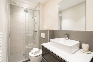 Een moderne badkamer met een glazen douchecabine, een wit wastafelmeubel en een toilet.