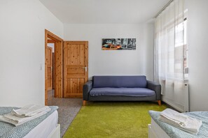 Une pièce comprenant un lit, un canapé, une porte en bois, un tableau au mur et une fenêtre avec des rideaux.